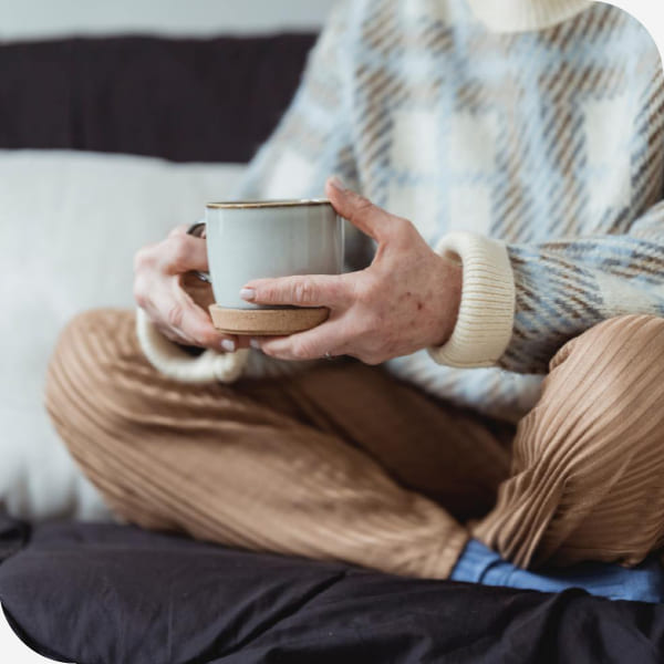 primer plano de las manos de una mujer sentada con las piernas cruzadas mientras sostiene su taza de café