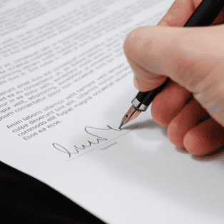 Primer plano de una mano estampando una firma con una pluma en un documento