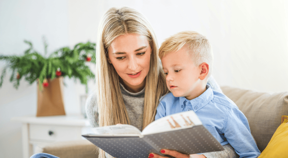 Madrd joven con su hijo de tres años leyendo un libro en el sofá