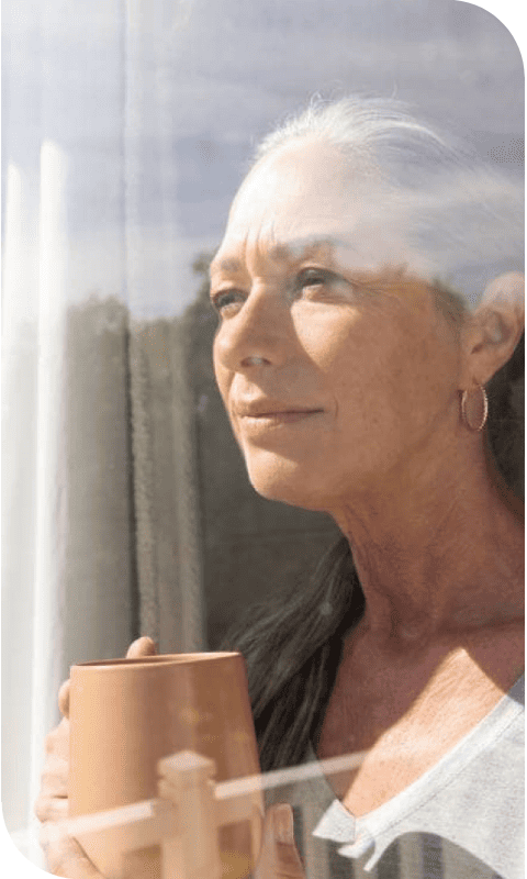 Mujer mirando por la ventana mientras bebe una taza de té